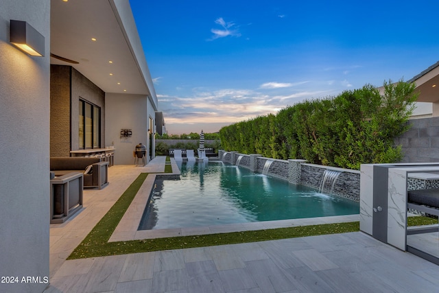 pool at dusk with pool water feature, an outdoor kitchen, and a patio