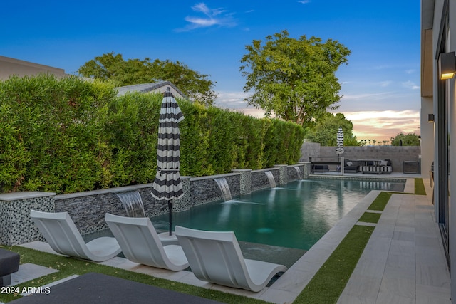 pool at dusk with pool water feature and a patio area