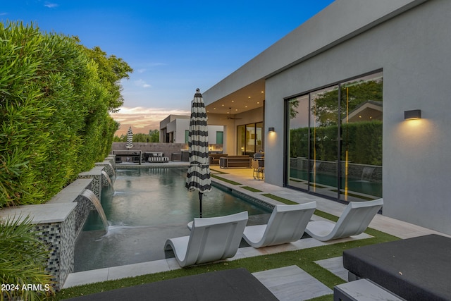 pool at dusk with pool water feature and a patio