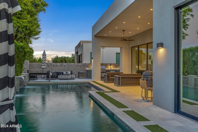 pool at dusk with a patio area, pool water feature, ceiling fan, an outdoor hangout area, and an outdoor kitchen