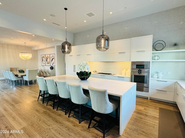 kitchen featuring white cabinets, pendant lighting, a large island, and light hardwood / wood-style flooring