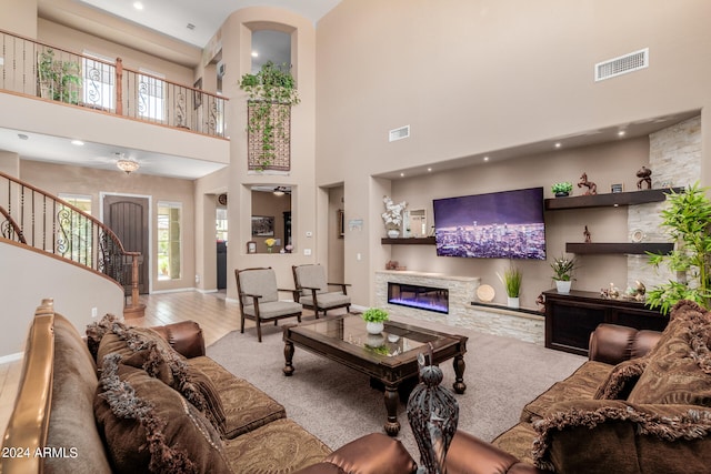 living room with ceiling fan, a fireplace, a high ceiling, and light hardwood / wood-style flooring