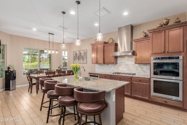 kitchen with sink, wall chimney exhaust hood, a kitchen breakfast bar, decorative light fixtures, and a kitchen island with sink