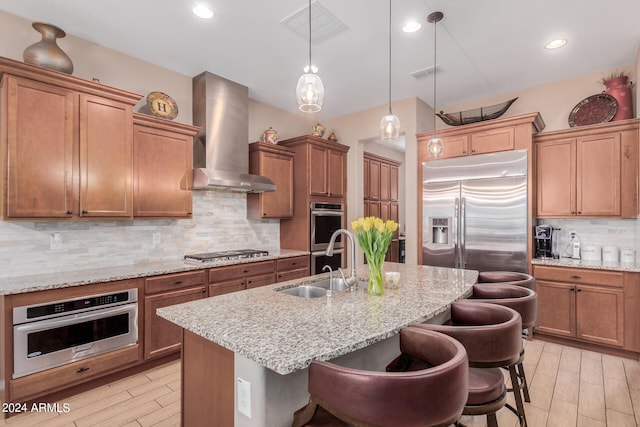 kitchen with a kitchen island with sink, a breakfast bar, stainless steel appliances, and wall chimney range hood