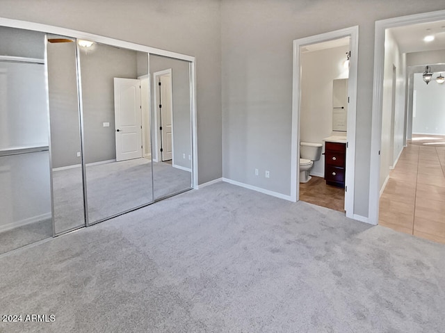 unfurnished bedroom with ensuite bathroom, a closet, and light colored carpet