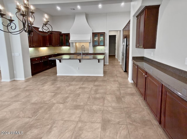 kitchen featuring premium range hood, decorative backsplash, stainless steel fridge, a breakfast bar area, and a chandelier