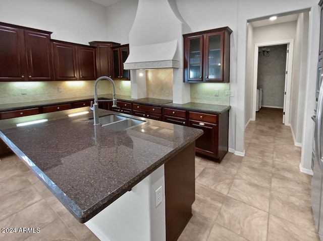 kitchen featuring decorative backsplash, sink, dark stone counters, and an island with sink