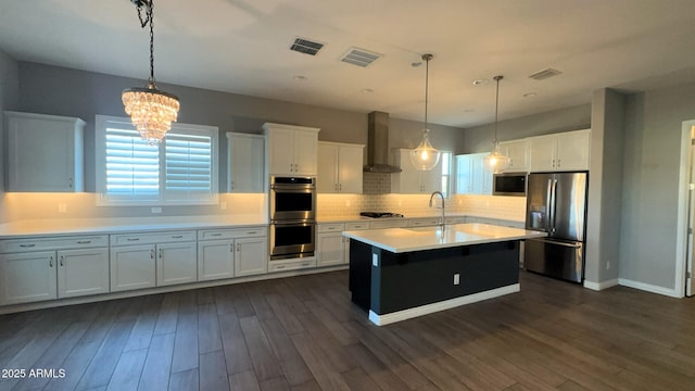 kitchen featuring white cabinets, appliances with stainless steel finishes, decorative light fixtures, and wall chimney range hood