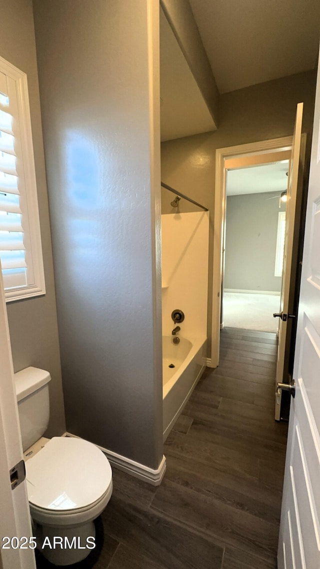 bathroom with hardwood / wood-style floors, toilet, and washtub / shower combination