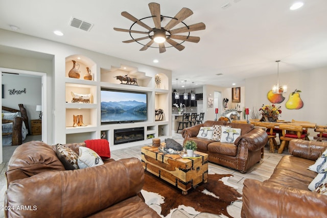 living room with built in shelves, ceiling fan with notable chandelier, and light tile patterned flooring