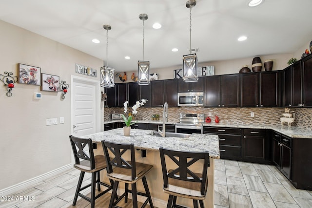 kitchen with a kitchen bar, light stone countertops, stainless steel appliances, a kitchen island with sink, and decorative light fixtures