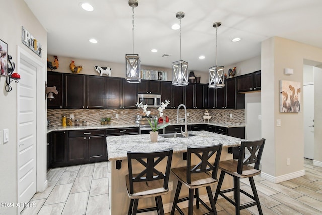 kitchen featuring sink, an island with sink, appliances with stainless steel finishes, tasteful backsplash, and a breakfast bar area