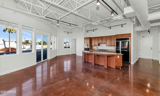 kitchen featuring sink, a breakfast bar area, a center island with sink, black refrigerator, and a high ceiling