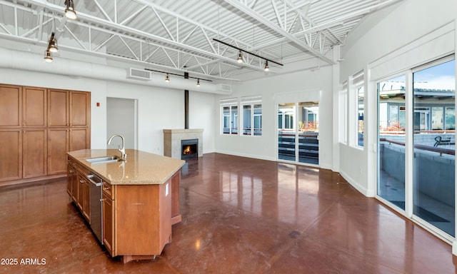 kitchen featuring a fireplace, dishwasher, an island with sink, sink, and light stone countertops