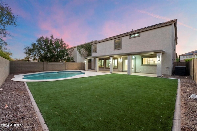 back house at dusk with a fenced in pool, a patio area, a yard, and cooling unit