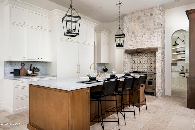 kitchen with light stone countertops, tasteful backsplash, decorative light fixtures, a center island with sink, and white cabinetry