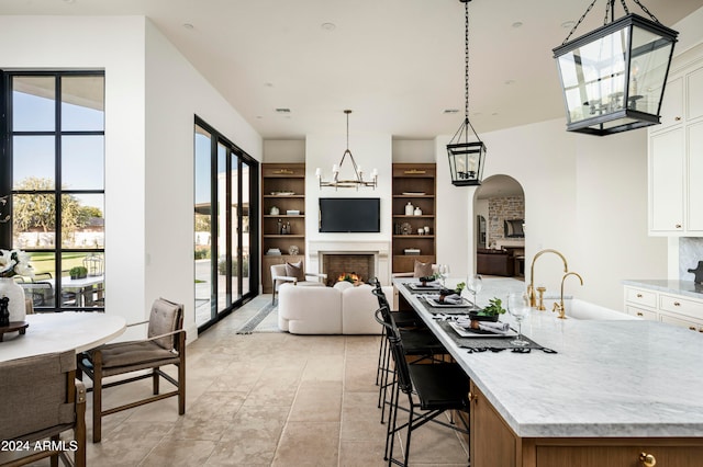 kitchen with light stone countertops, a kitchen island with sink, sink, white cabinetry, and hanging light fixtures