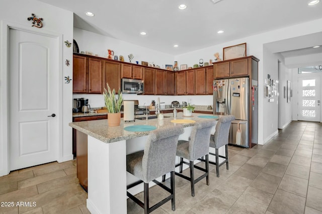 kitchen featuring stainless steel appliances, light stone countertops, a breakfast bar, and a center island with sink