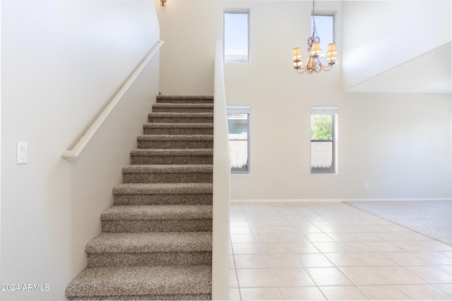 staircase with a notable chandelier, a towering ceiling, and tile patterned floors