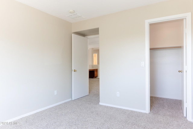 unfurnished bedroom with a spacious closet, light colored carpet, and a closet