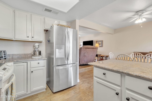 kitchen featuring stove, light stone counters, stainless steel fridge, and white cabinets