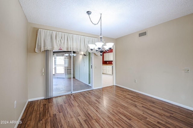 unfurnished dining area with hardwood / wood-style floors, a textured ceiling, and a notable chandelier