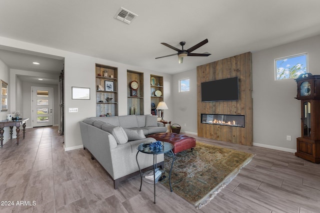 living room featuring light hardwood / wood-style floors, ceiling fan, a large fireplace, and plenty of natural light