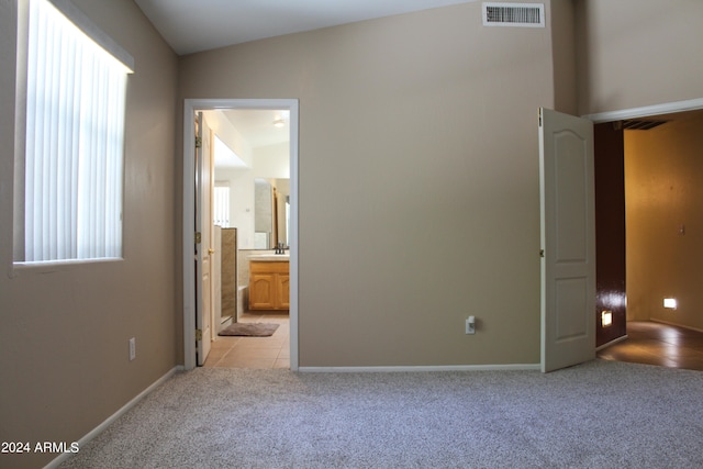 unfurnished bedroom with light carpet, lofted ceiling, multiple windows, and ensuite bath