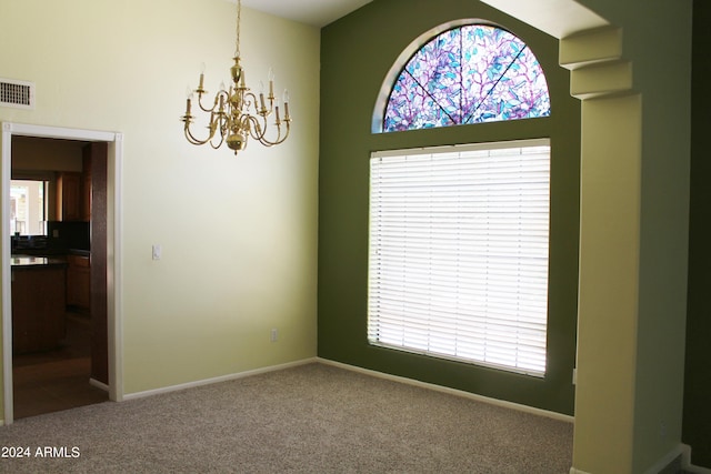 carpeted empty room with a wealth of natural light, a chandelier, and a high ceiling