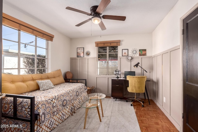 sitting room with wainscoting, a decorative wall, and ceiling fan