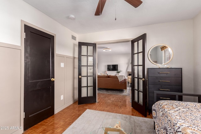 bedroom with visible vents, a ceiling fan, a wainscoted wall, french doors, and a decorative wall