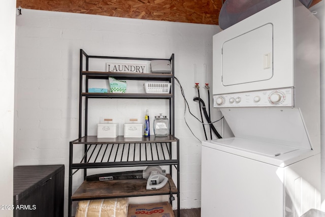 laundry room with concrete block wall, stacked washing maching and dryer, and laundry area