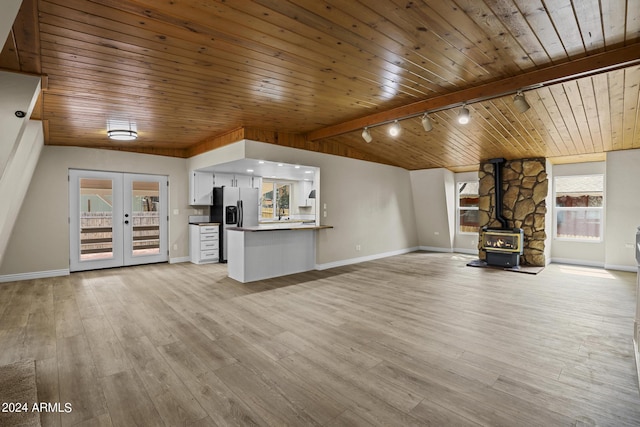 unfurnished living room featuring french doors, light wood finished floors, wood ceiling, a wood stove, and vaulted ceiling