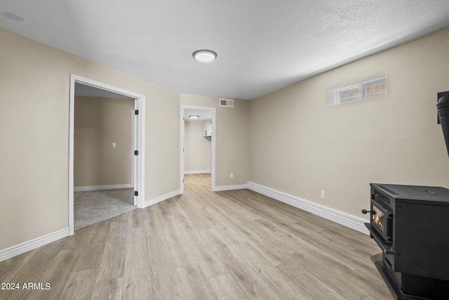 unfurnished living room featuring a textured ceiling, light wood-type flooring, and a wood stove