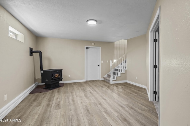 basement featuring a textured ceiling, light hardwood / wood-style floors, and a wood stove