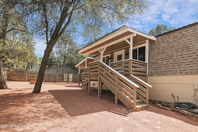 view of exterior entry featuring a patio, roof with shingles, and fence