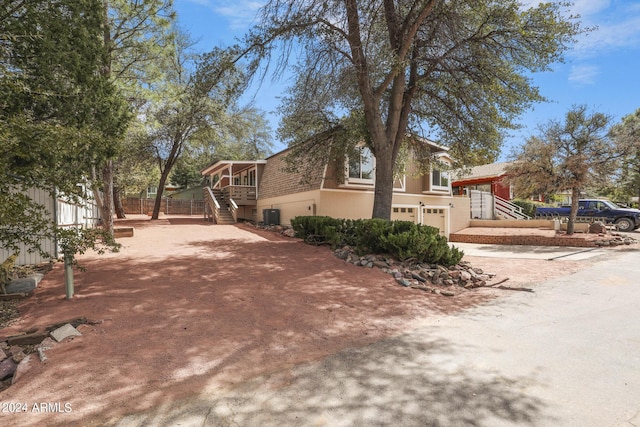 view of side of home with central AC, roof with shingles, stucco siding, a garage, and driveway