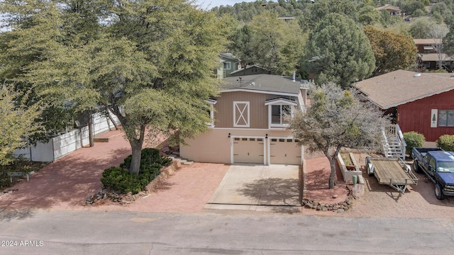 view of property hidden behind natural elements with stucco siding, concrete driveway, an attached garage, and fence