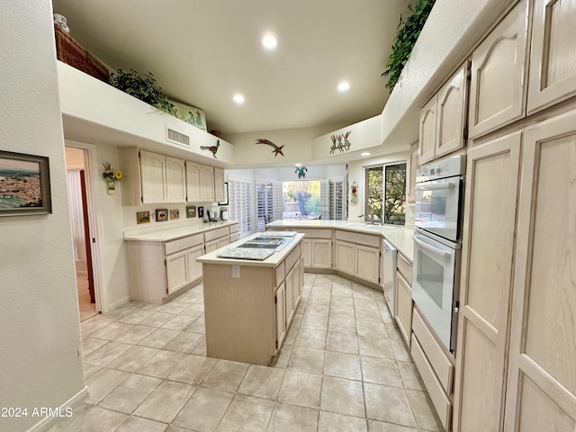 kitchen with dishwasher, sink, kitchen peninsula, light brown cabinetry, and a kitchen island