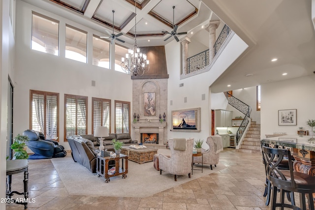 living room with ceiling fan with notable chandelier, a high ceiling, a large fireplace, beam ceiling, and coffered ceiling