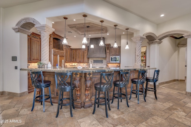 kitchen with stainless steel microwave, premium range hood, pendant lighting, kitchen peninsula, and decorative columns