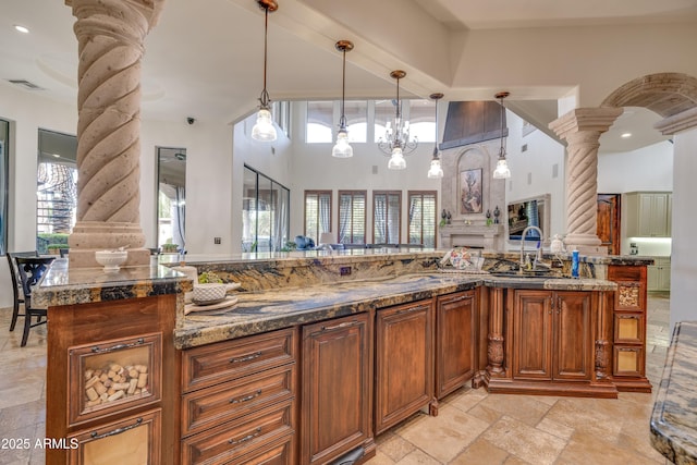 kitchen featuring ornate columns, a notable chandelier, hanging light fixtures, rustic walls, and sink