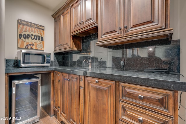 kitchen with sink, beverage cooler, dark stone counters, and tasteful backsplash