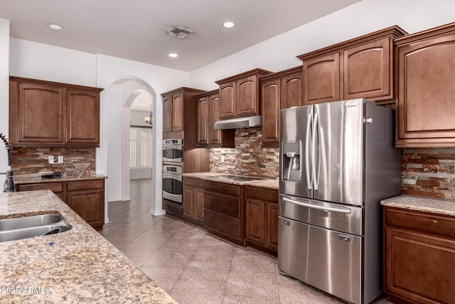 14552 S 182nd Dr, Goodyear, AZ 85338 - kitchen with appliances with stainless steel finishes, tasteful backsplash, arched walkways, under cabinet range hood, and light tile patterned flooring