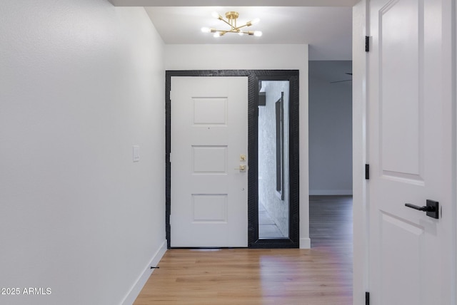 entryway featuring light wood finished floors, an inviting chandelier, and baseboards