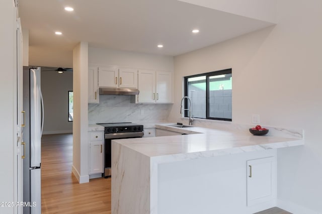 kitchen with under cabinet range hood, a peninsula, a sink, electric stove, and freestanding refrigerator