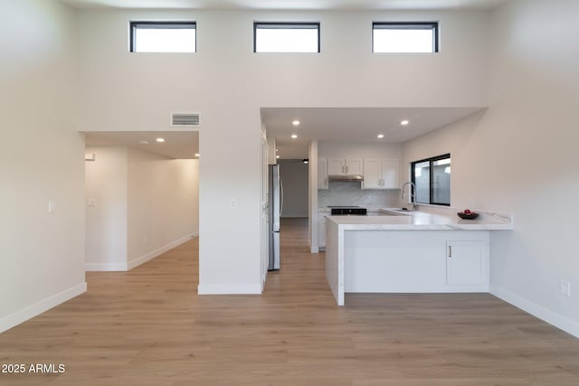 kitchen with a peninsula, a sink, visible vents, white cabinetry, and light countertops