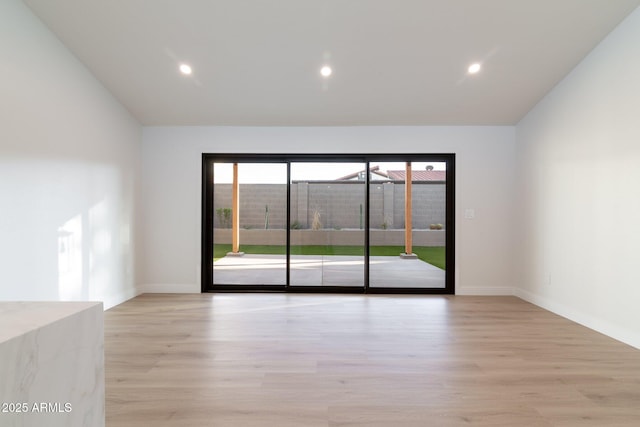 empty room with vaulted ceiling, light wood-style flooring, and baseboards