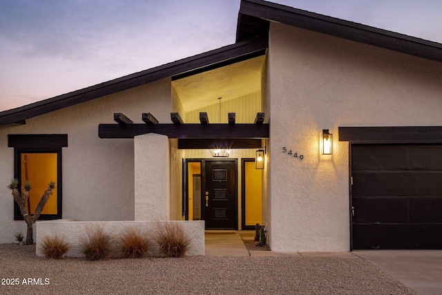 exterior entry at dusk featuring an attached garage and stucco siding