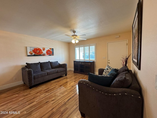 living room with a textured ceiling, ceiling fan, and light hardwood / wood-style flooring